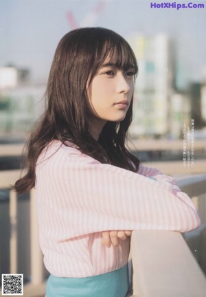 A woman in a pink sweater and blue skirt standing on a balcony.