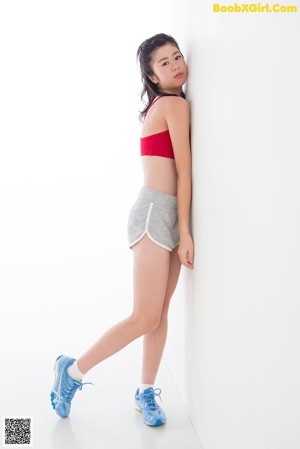 A woman in a red sports bra top and gray shorts standing on a scale.