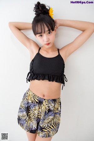 A woman in a black top and yellow shorts leaning against a wall.