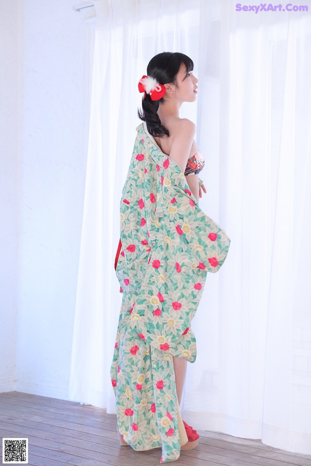 A woman in a green and red kimono standing in front of a window.