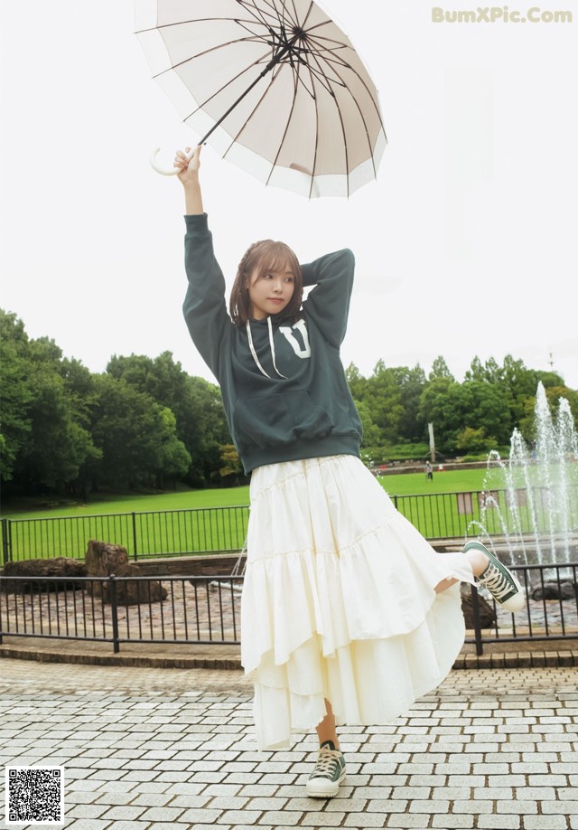 A woman in a green sweatshirt and white skirt holding an umbrella.