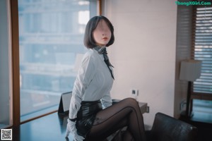 A woman in a white shirt and black leather skirt sitting on a chair.