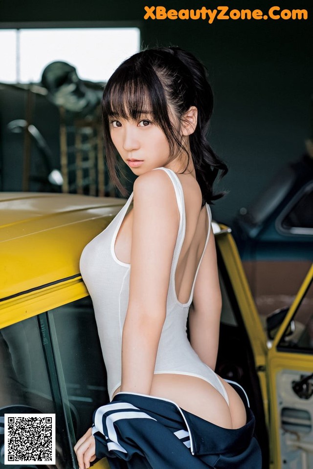 A woman in a white bodysuit leaning against a yellow car.