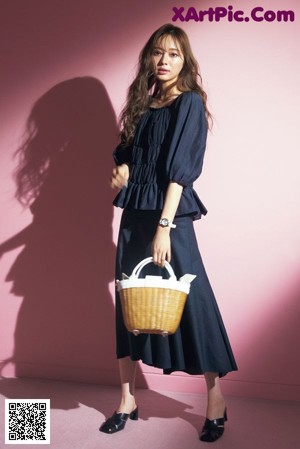 A woman in a black top and shorts holding a red bag.