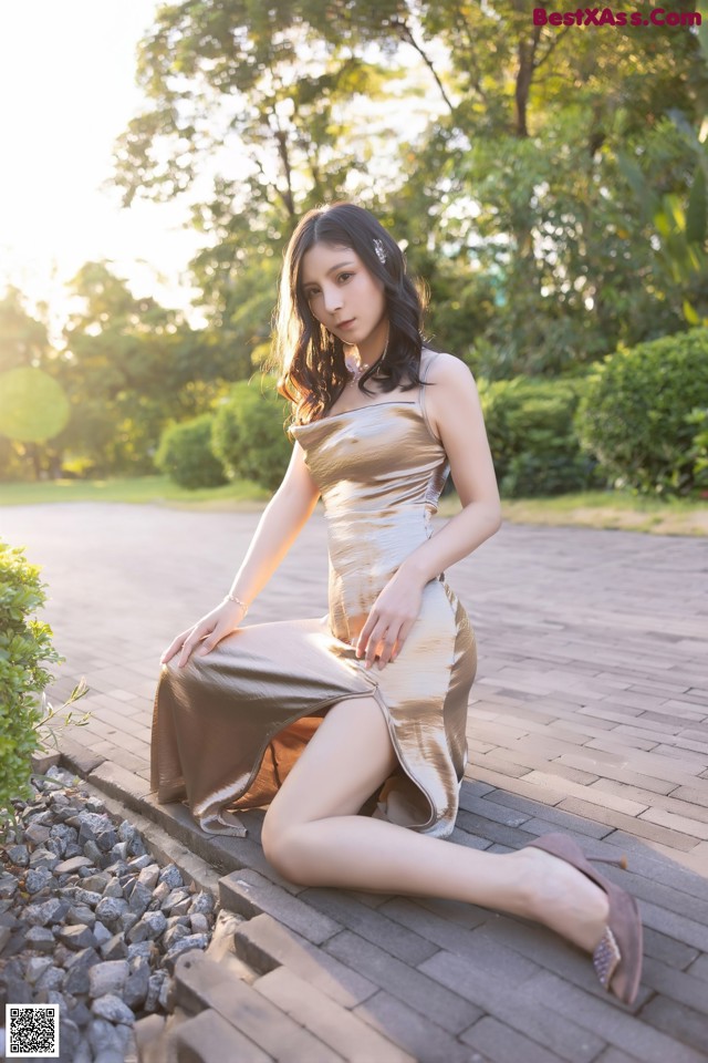 A woman in a gold dress sitting on a brick walkway.