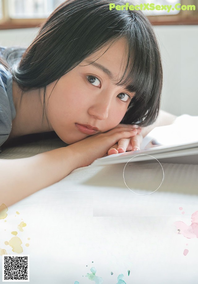 A young woman laying on top of a bed next to a book.