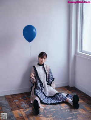 A woman standing in front of a window holding a bunch of balloons.