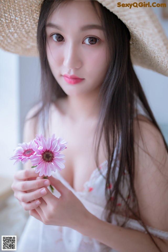 A woman in a straw hat holding a pink flower.