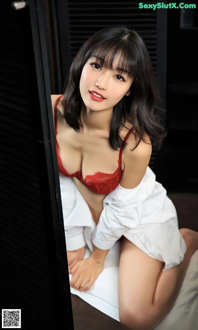 A woman in a red bra and white shirt sitting on a bed.