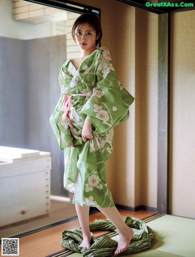 A woman in a green kimono standing on a tatami mat.