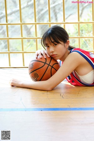 A woman sitting on the floor holding a basketball.