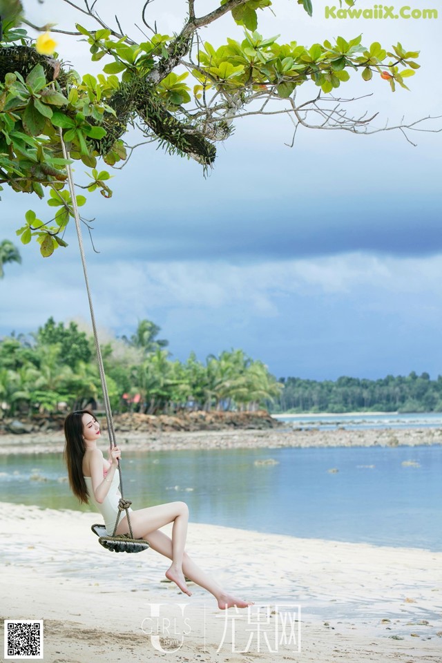 A woman sitting on a swing on a beach.