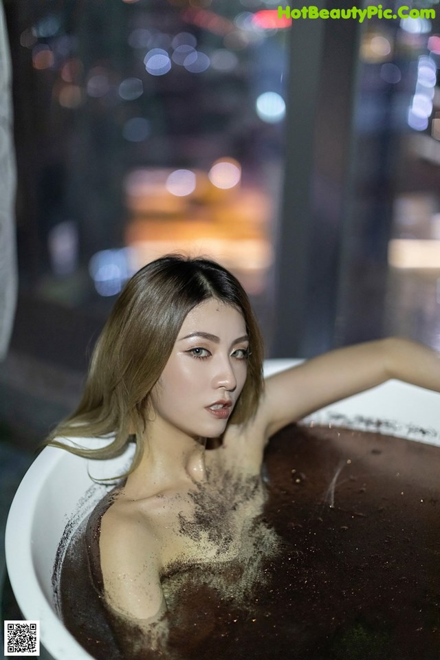 A woman sitting in a bathtub filled with brown liquid.