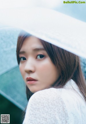 A woman in a white dress holding an umbrella in the rain.