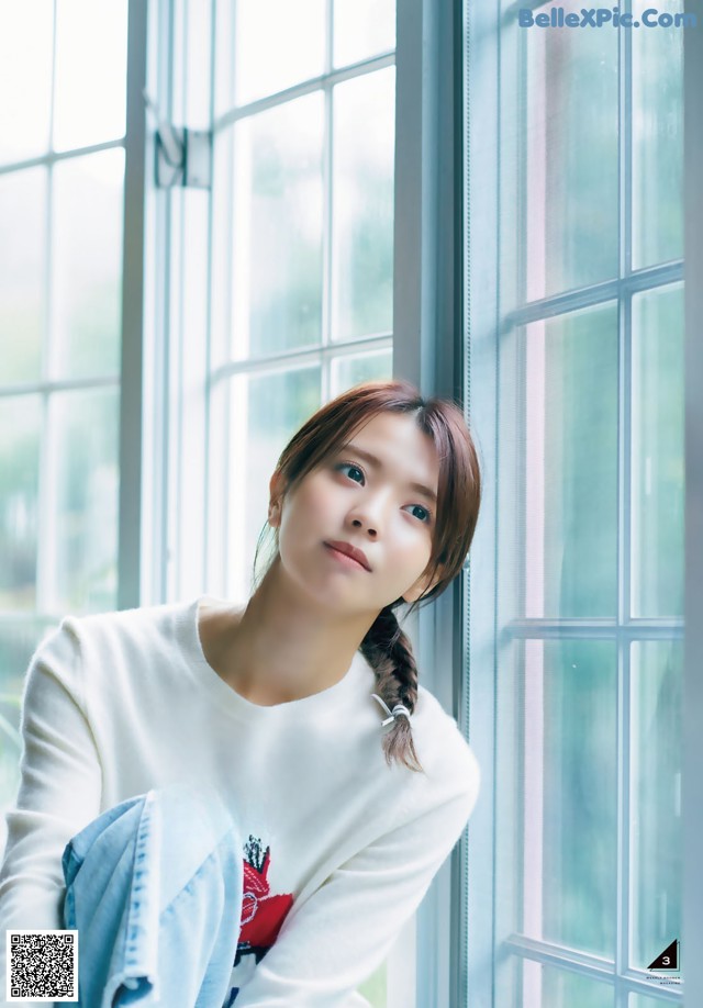 A woman sitting in front of a window wearing a white shirt.