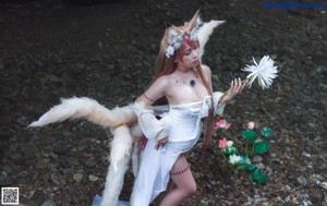 A woman in a white dress sitting on a rock next to a white wolf.