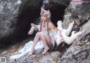 A woman in a white dress sitting on a rock next to a white fox.